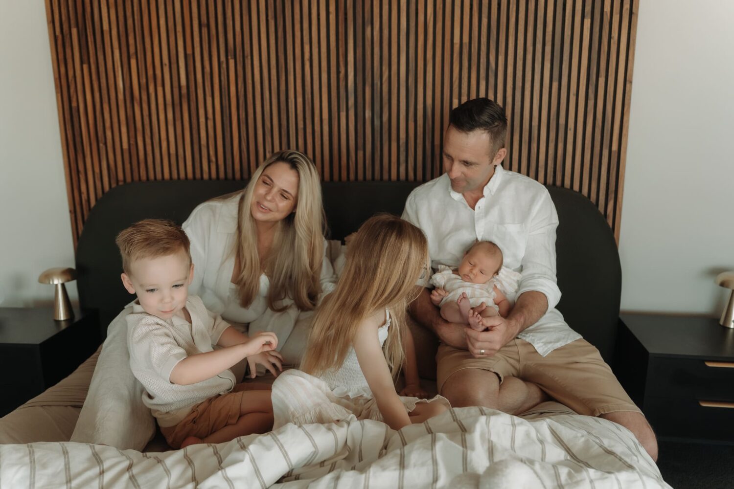 Family cuddling together on a bed, admiring their newborn baby and sibling.